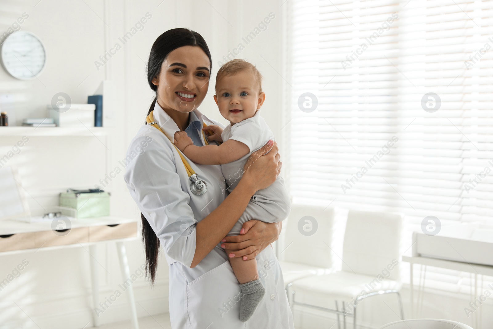 Photo of Young pediatrician with cute little baby in clinic. Space for text