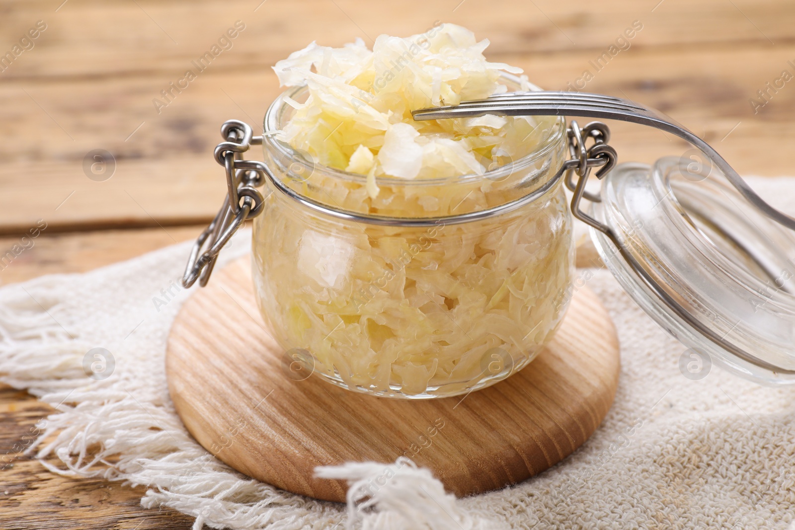 Photo of Glass jar of tasty sauerkraut on wooden table, closeup