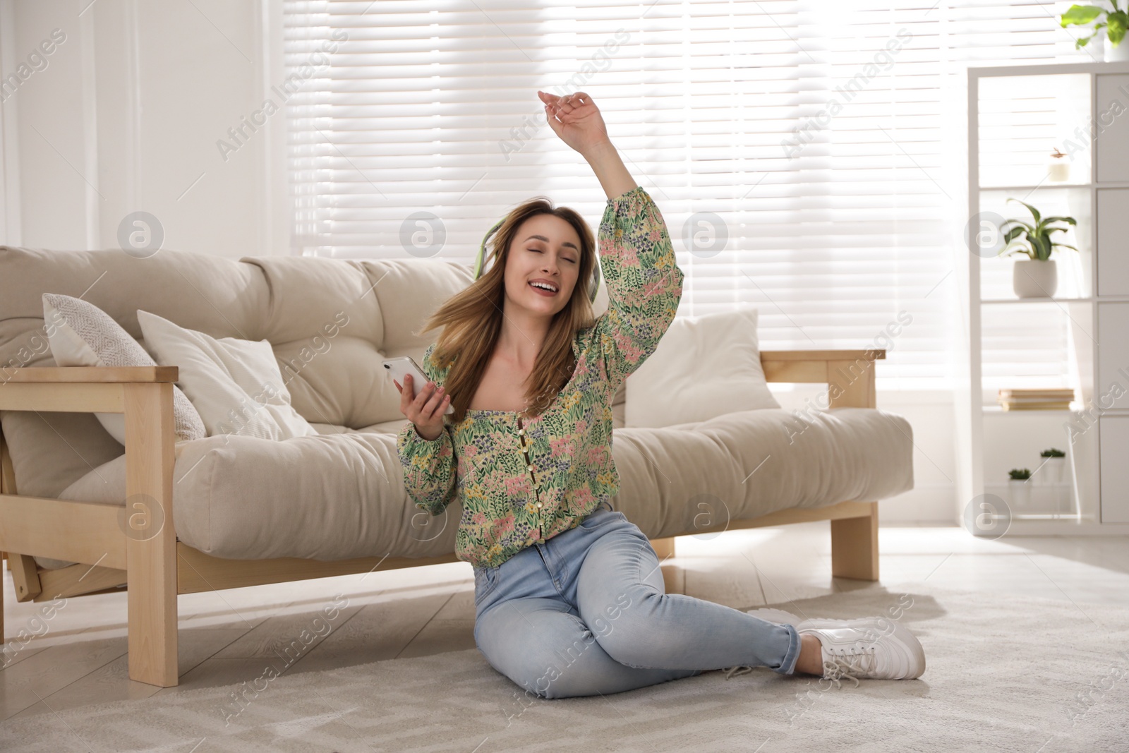 Photo of Young woman with headphones listening to music while sitting on floor in living room