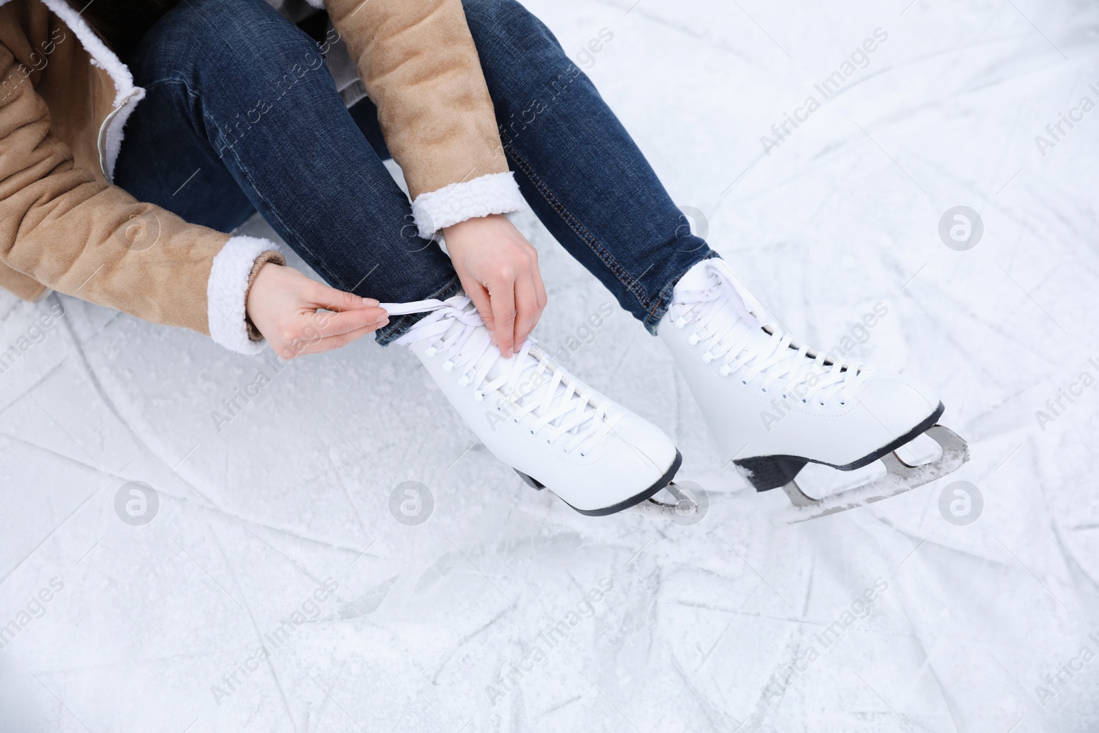 Photo of Woman lacing figure skate while sitting on ice, closeup