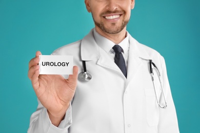 Photo of Male doctor holding card with word UROLOGY on turquoise background, closeup