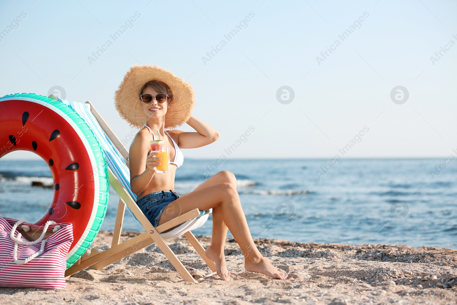 Photo of Young woman with cocktail in beach chair at seacoast. Space for text