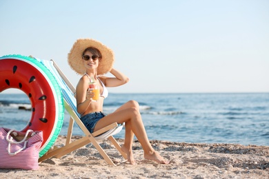 Young woman with cocktail in beach chair at seacoast. Space for text