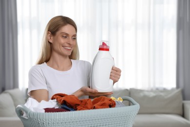 Photo of Woman holding fabric softener and basket with dirty clothes in room, space for text
