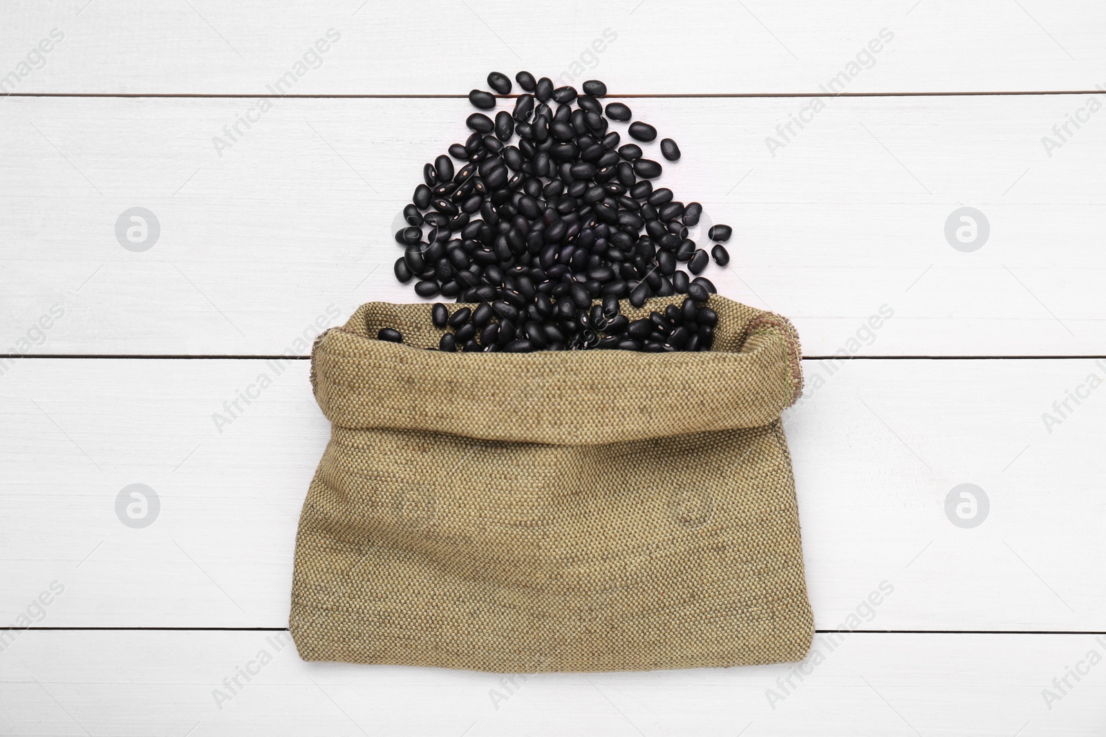 Photo of Sack of raw black beans on white wooden table, top view