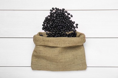 Photo of Sack of raw black beans on white wooden table, top view