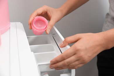 Photo of Woman pouring laundry detergent into drawer of washing machine, closeup