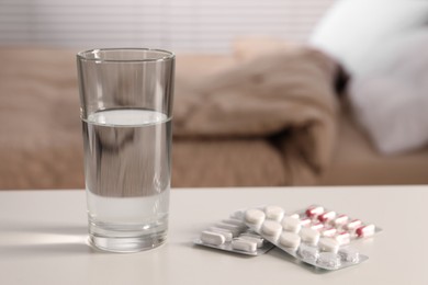 Photo of Glass of water and different pills in blisters on white table indoors, space for text