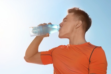 Photo of Young sporty man drinking water from bottle against blue sky on sunny day