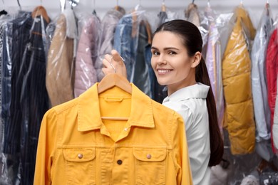 Dry-cleaning service. Happy worker holding hanger with jacket indoors