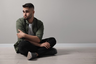 Photo of Sad man sitting on floor near light grey wall. Space for text