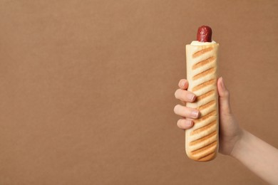 Woman holding delicious french hot dog on brown background, closeup. Space for text