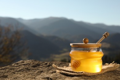 Photo of Fresh aromatic honey in glass jar on rock against mountain landscape. Space for text