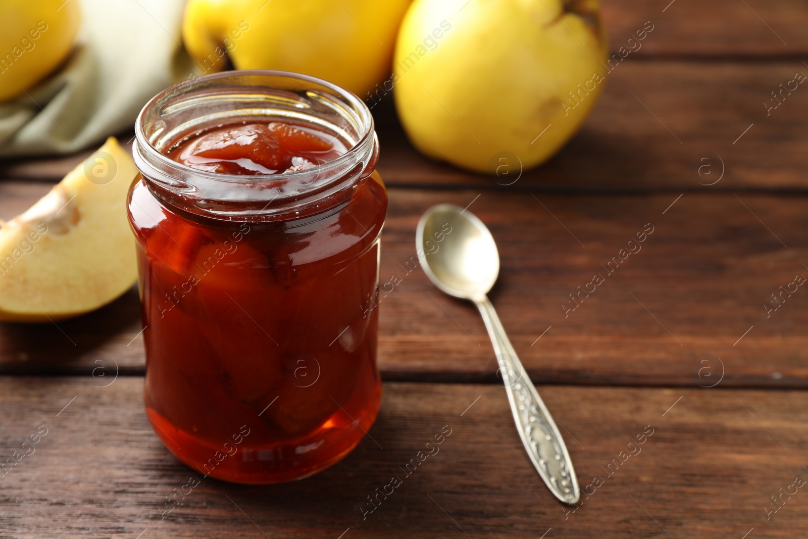 Photo of Tasty homemade quince jam in jar on wooden table, closeup. Space for text