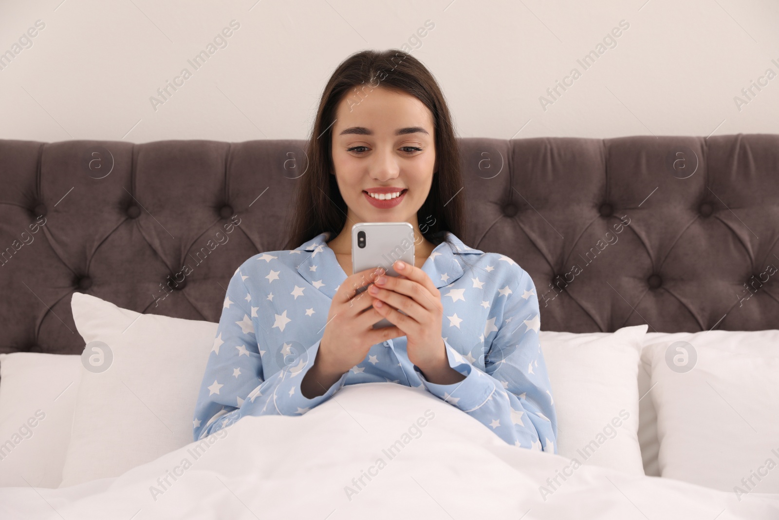 Photo of Young woman addicted to smartphone in bed at home