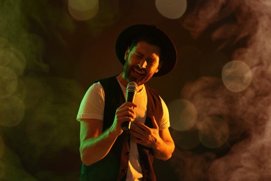 Image of Handsome man with microphone singing on stage in color lighted smoke