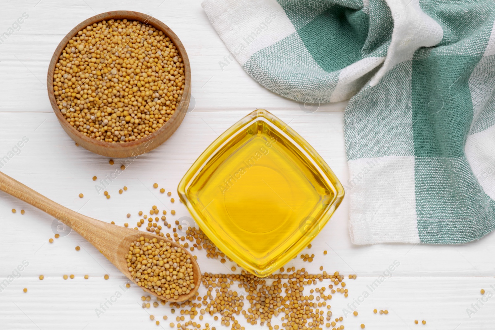 Bowl of natural oil and mustard seeds on white wooden table, flat lay Photo of Bowl of natural oil and mustard seeds on white wooden table, flat lay