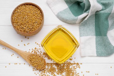 Photo of Bowl of natural oil and mustard seeds on white wooden table, flat lay