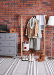 Photo of Beautiful hallway interior with coat rack and chest of drawers near red brick wall