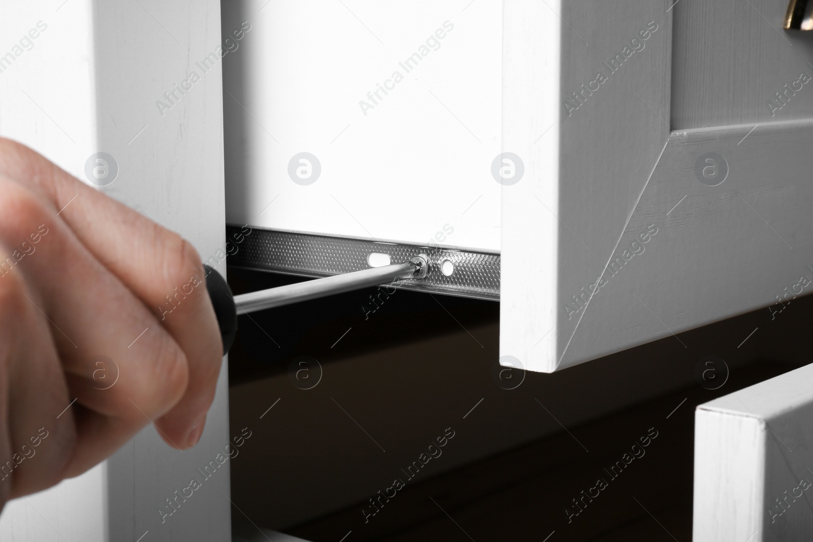 Photo of Man fixing drawer of white wardrobe with screwdriver, closeup