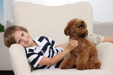 Photo of Little child with cute puppy in armchair indoors. Lovely pet