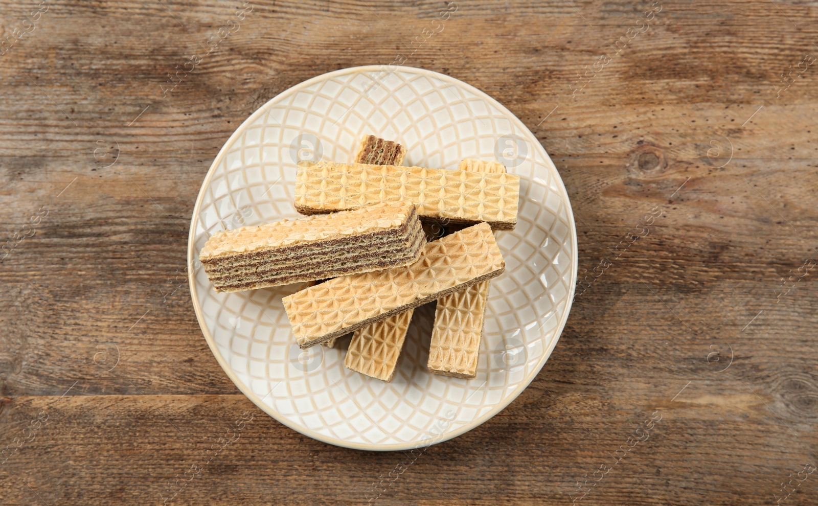 Photo of Plate of delicious wafers on brown wooden background, top view