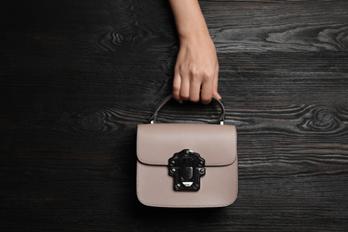 Photo of Woman holding small bag on black wooden background, top view