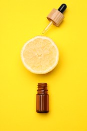 Photo of Bottle of citrus essential oil and fresh lemon on yellow background, flat lay