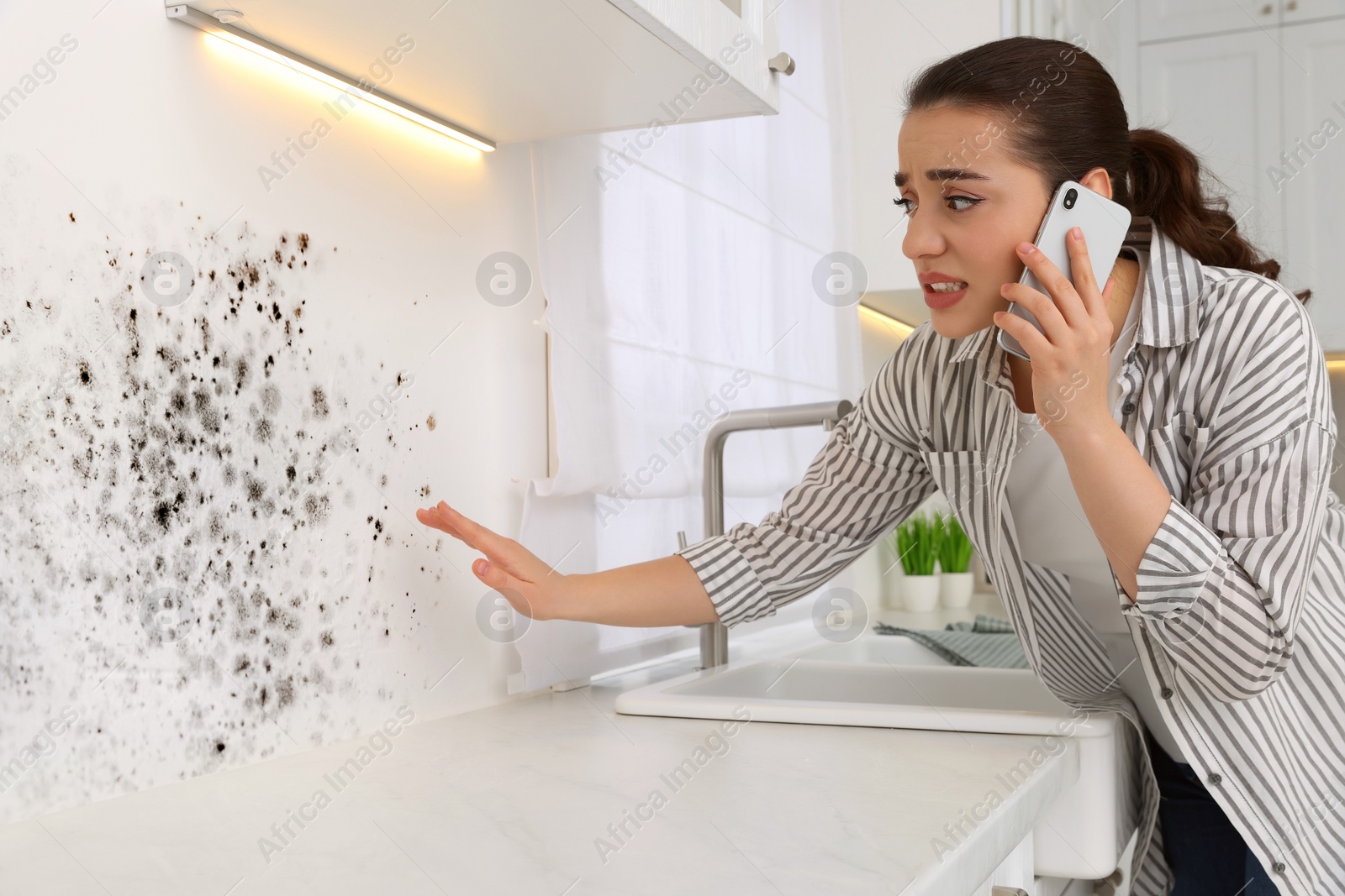 Image of Mold removal service. Woman talking on phone and looking at affected wall in kitchen