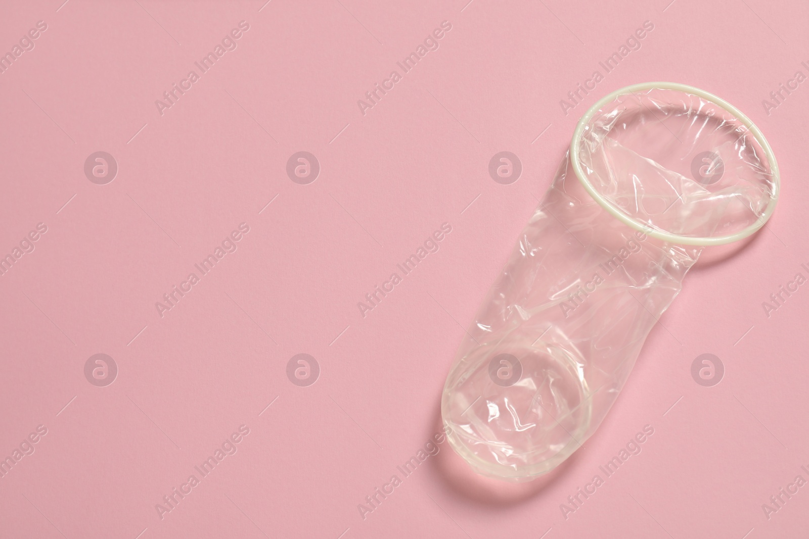 Photo of Unrolled female condom on light pink background, top view and space for text. Safe sex