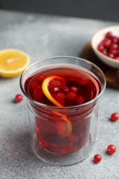 Photo of Tasty hot cranberry tea with lemon and fresh berries in glass on light grey textured table