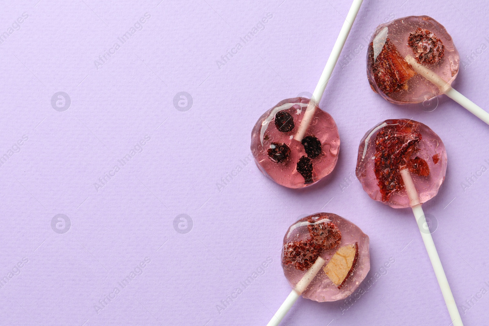 Photo of Sweet colorful lollipops with berries on lilac background, flat lay. Space for text