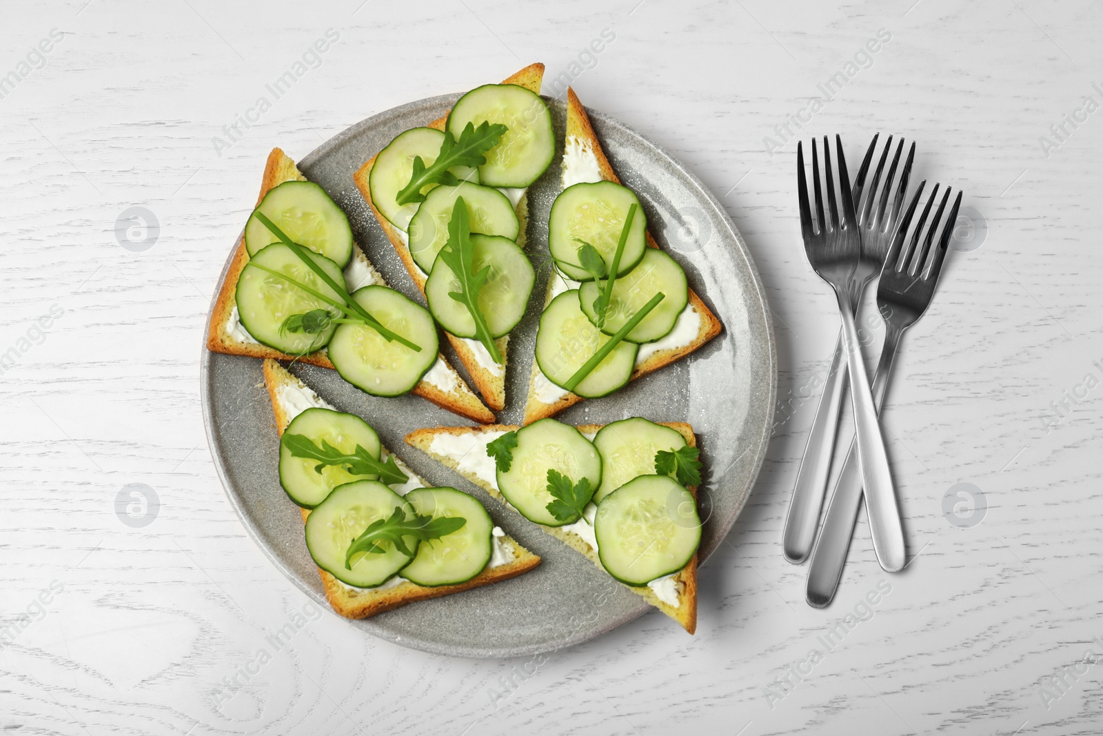 Photo of Plate with traditional English cucumber sandwiches and forks on white wooden background, top view