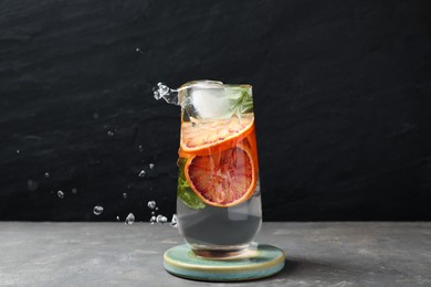 Photo of Delicious refreshing drink with sicilian orange splashing out of glass on grey table against black background