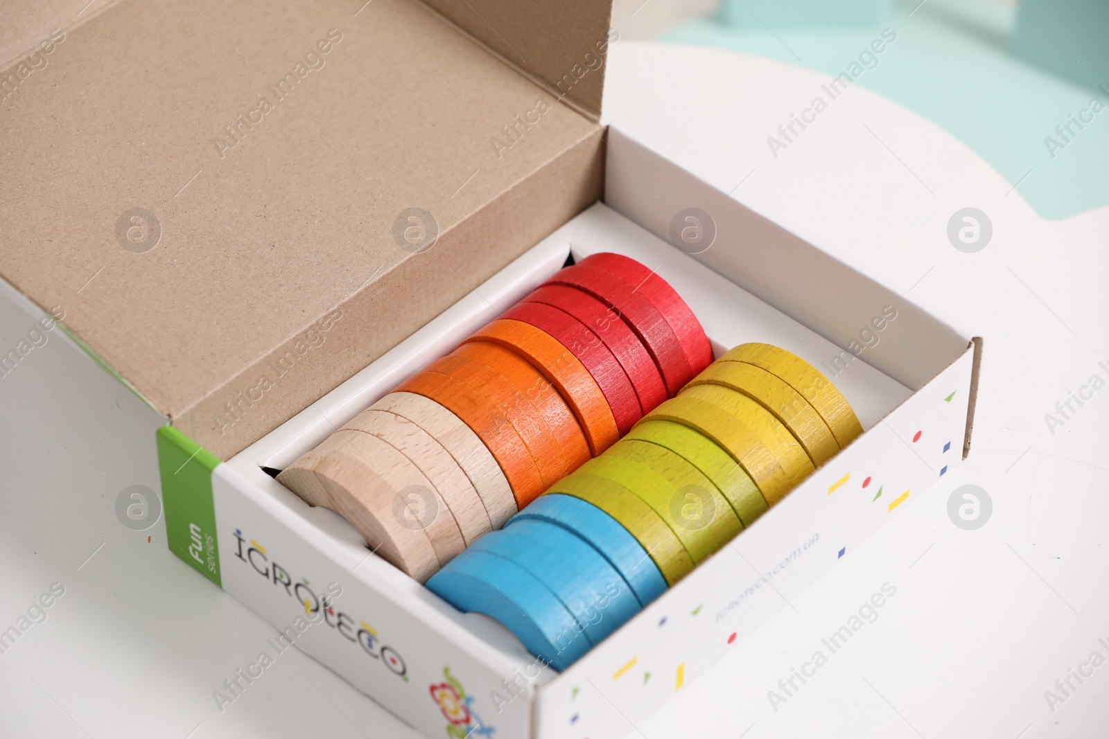 Photo of Box with colorful wooden pieces of playing set on white table, closeup. Educational toy for motor skills development