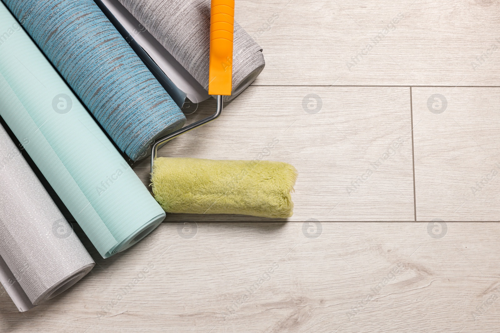 Photo of Different wallpaper rolls and roller on floor, top view. Space for text