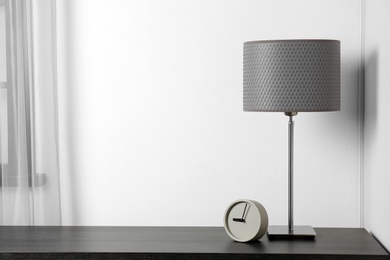 Stylish lamp and clock on table near white wall. Space for text