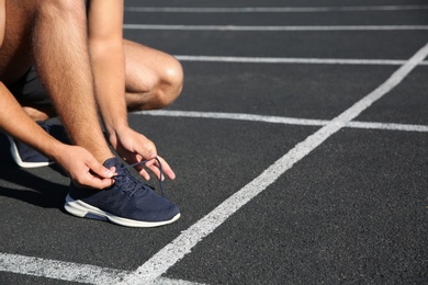 Sporty man tying shoelaces before running at stadium on sunny morning