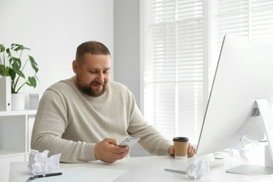 Photo of Lazy overweight office employee with smartphone at workplace