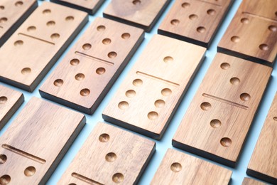 Photo of Wooden domino tiles on light blue background, closeup