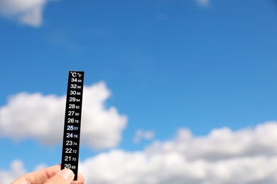 Photo of Woman holding weather thermometer against blue sky, closeup. Space for text