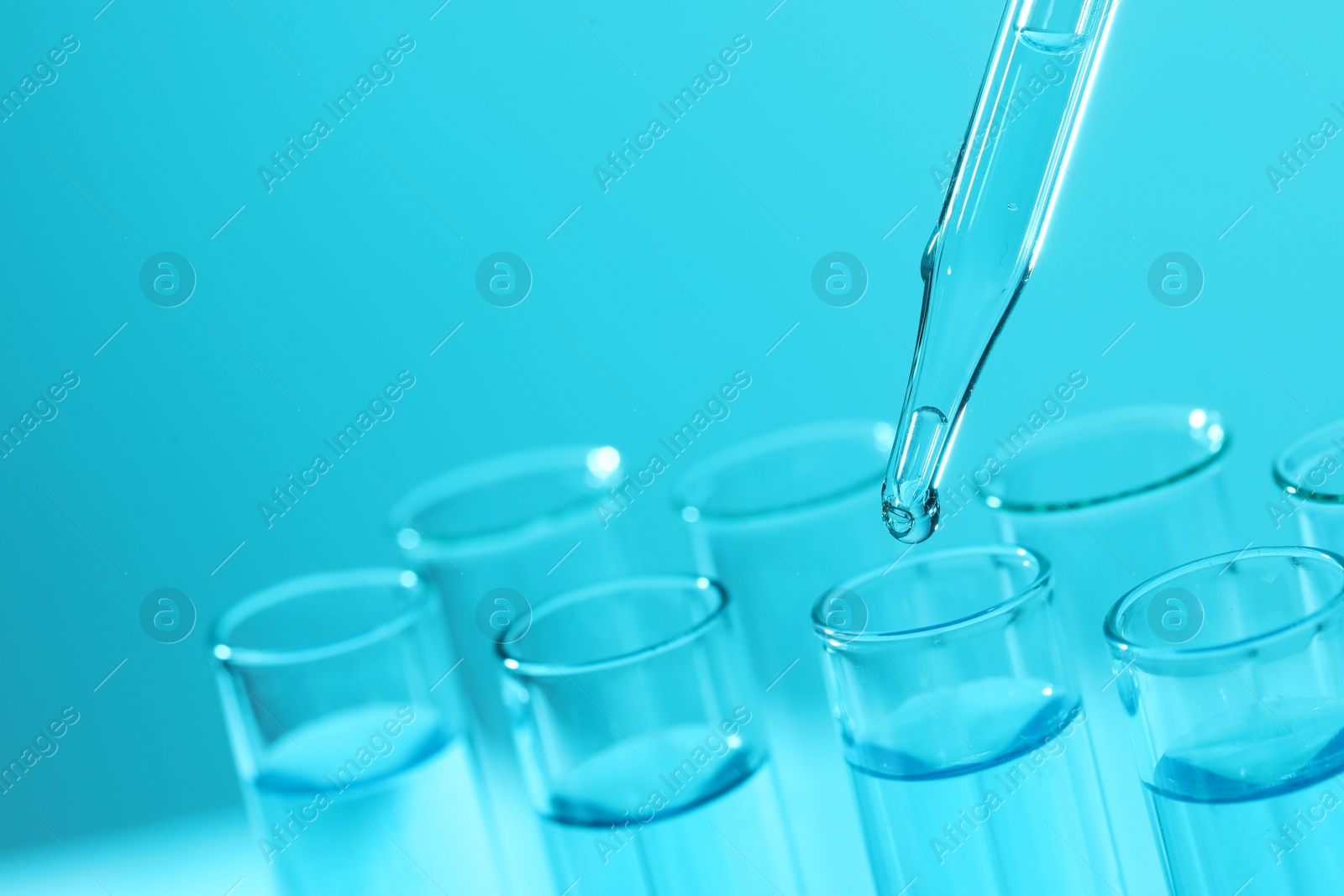 Photo of Dripping liquid from pipette into test tube on light blue background, closeup. Laboratory analysis