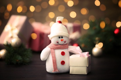 Image of Cute snowman with gift on table, bokeh effect