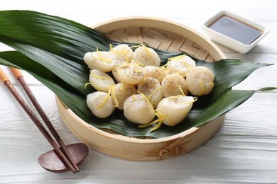 Raw scallops with milled pepper and lemon zest on white wooden table, closeup