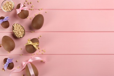 Photo of Sweet chocolate eggs and candies on pink wooden table, flat lay. Space for text