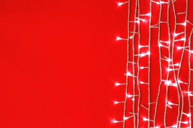 Photo of Christmas lights on red background, top view. Space for text