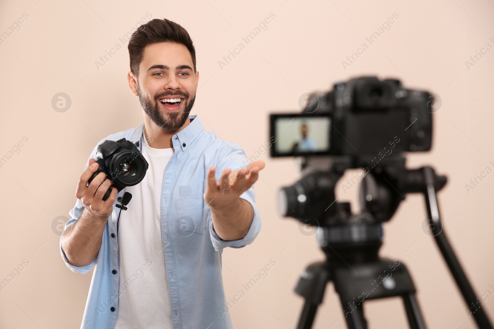 Photo of Young blogger with camera recording video against beige background