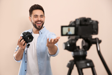 Young blogger with camera recording video against beige background