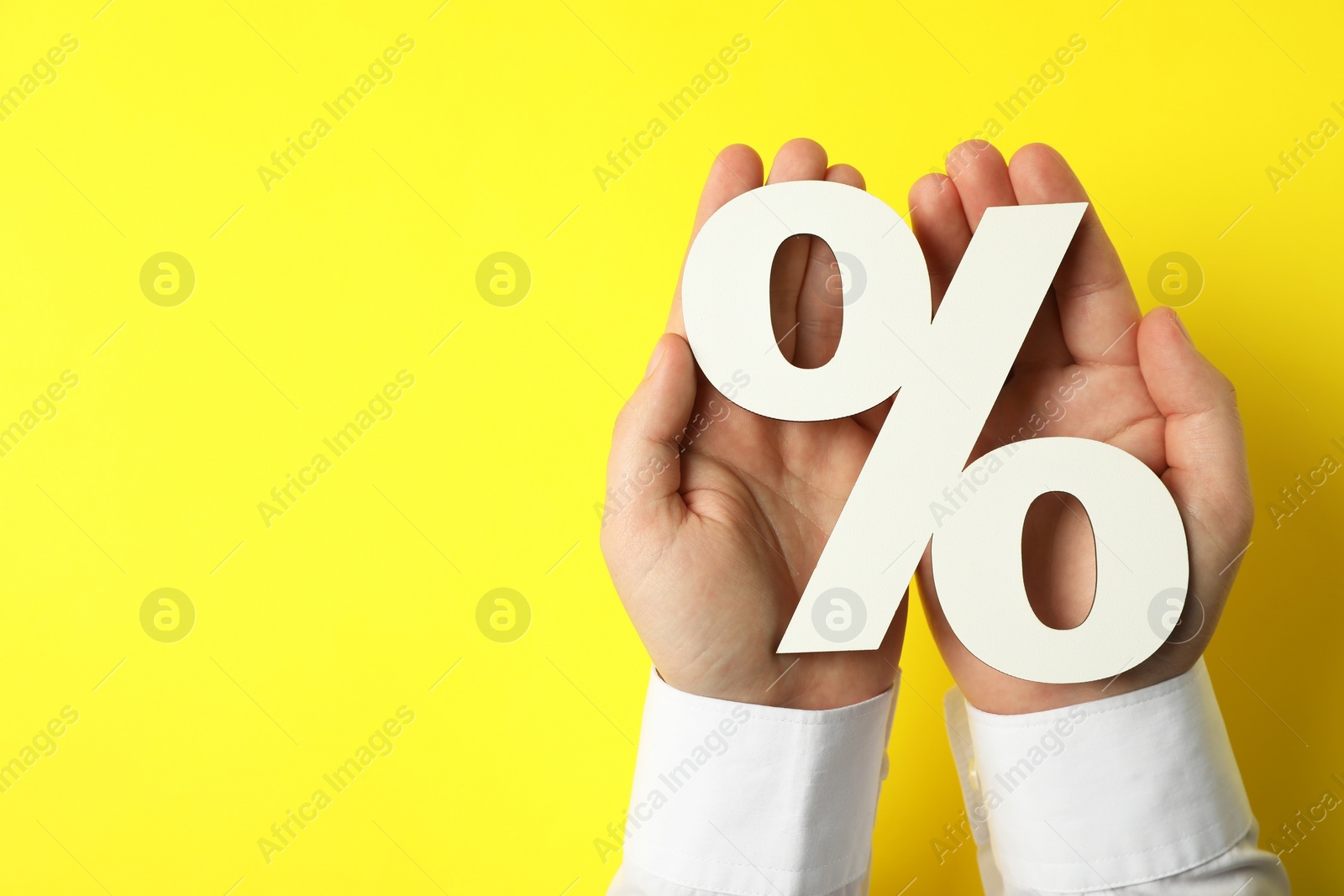 Photo of Man holding percent sign on yellow background, top view. Space for text