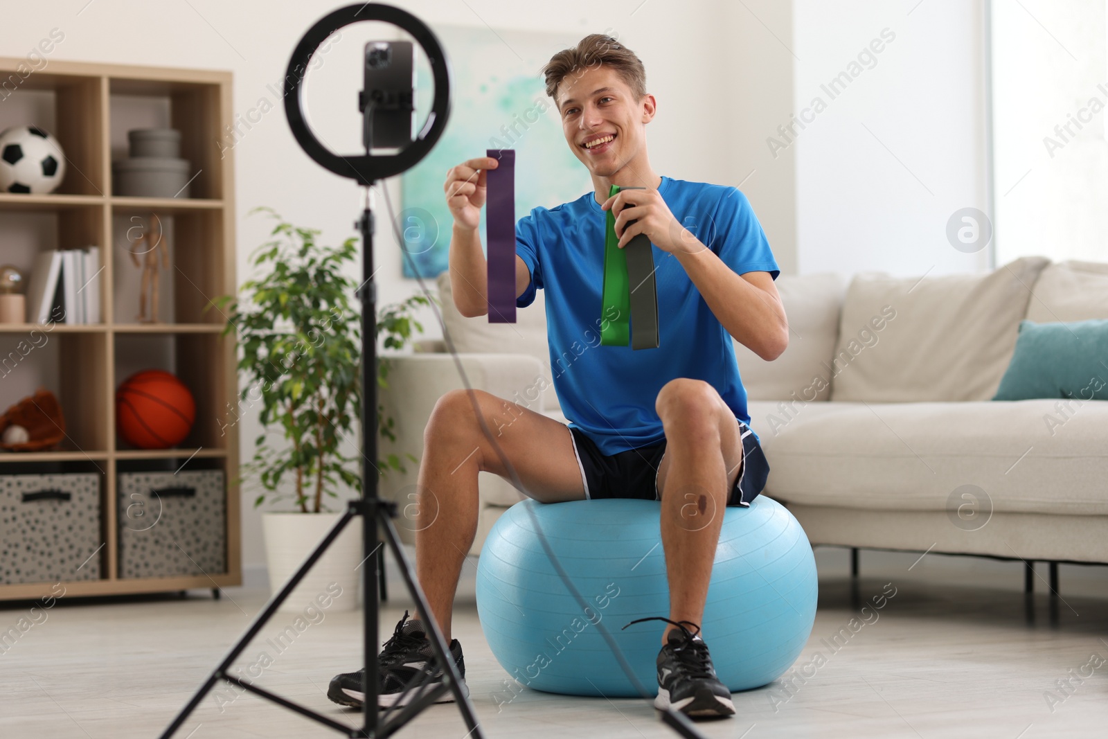 Photo of Smiling sports blogger with resistance bands streaming online fitness lesson at home